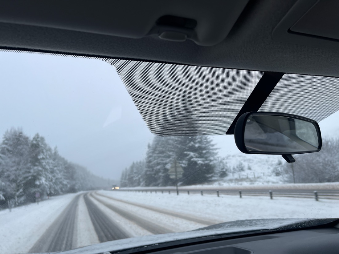 Winter road trip with snow from front car window in Scotland