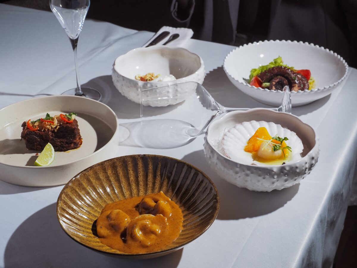 pexels 15701140 | Two Scots Abroad An elegant dining setup featuring gourmet dishes on a white tablecloth with glassware.