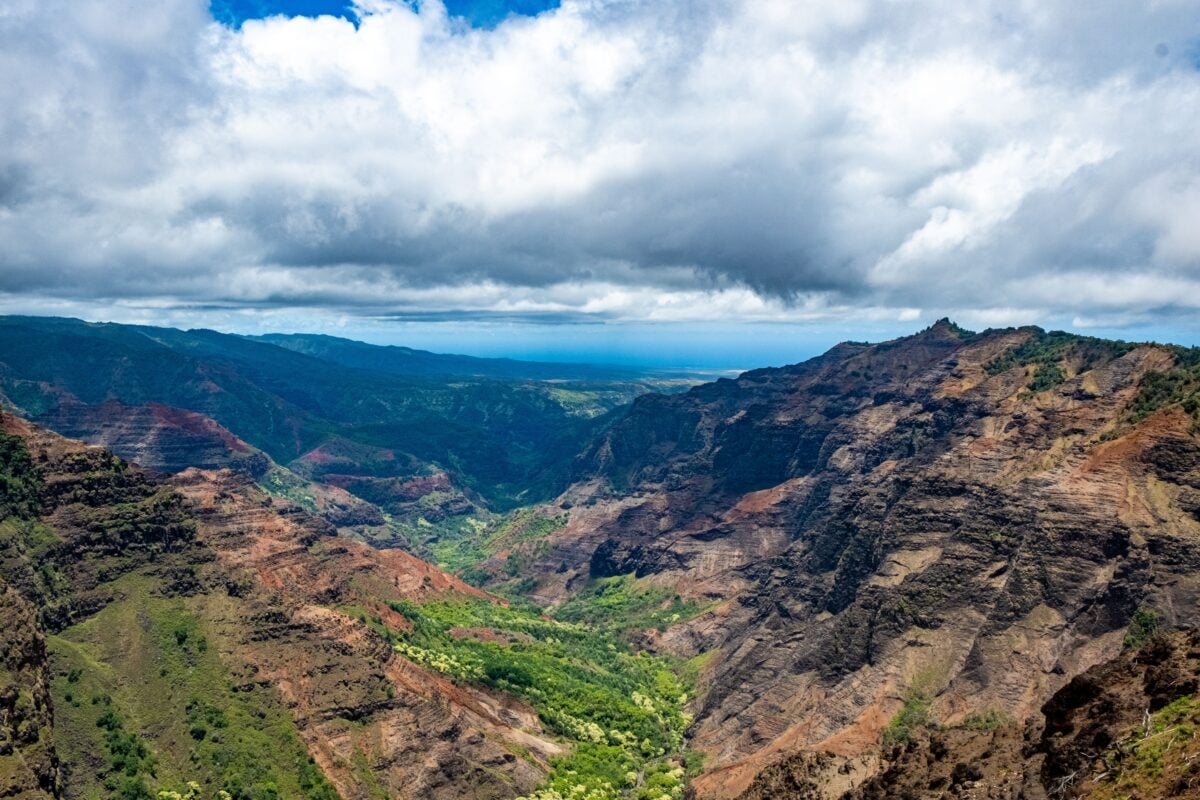 Stunning landscape view of Waimea Canyon, showcasing lush greenery and dramatic red cliffs under a cloudy sky.