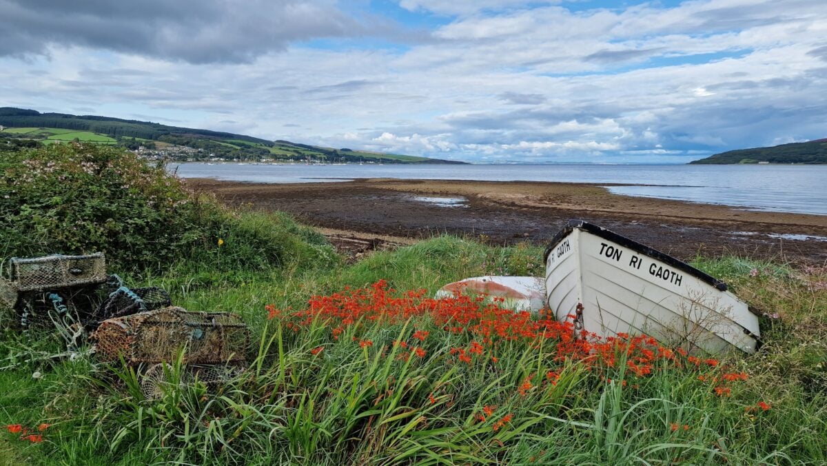 Tranquil view of a boat at Lamlash Bay, Scotland, surrounded by lush greenery and flowers.