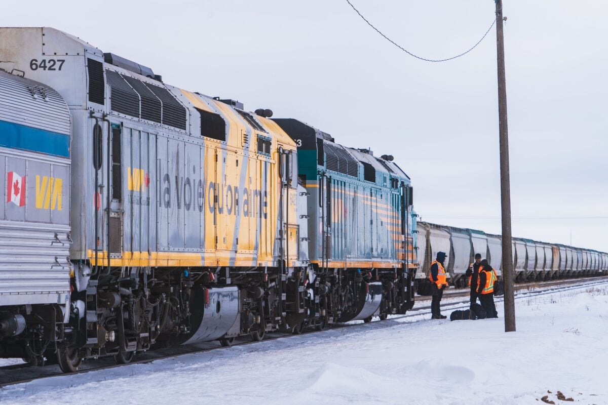 VIA Rail train crossing a snowy field in Canada during winter with railway workers.