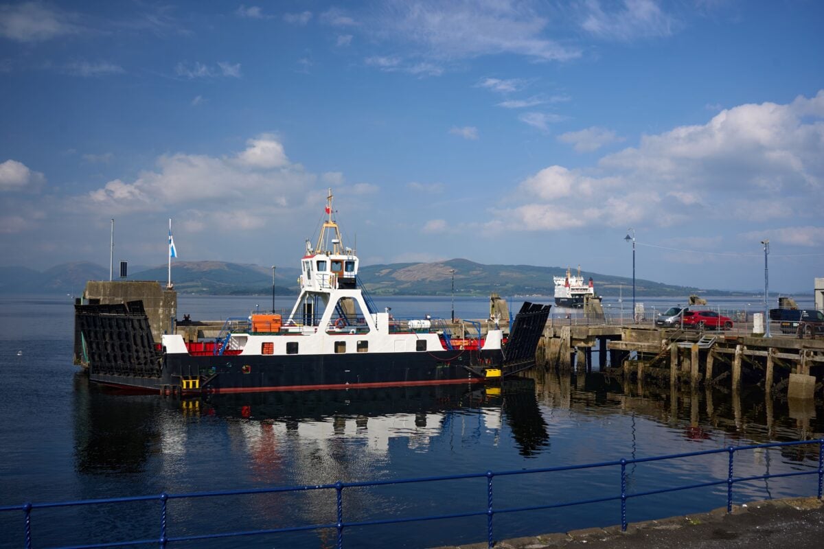 A ferry docked at the Isle of Bute harbor under a sunlit blue sky, Scotland.