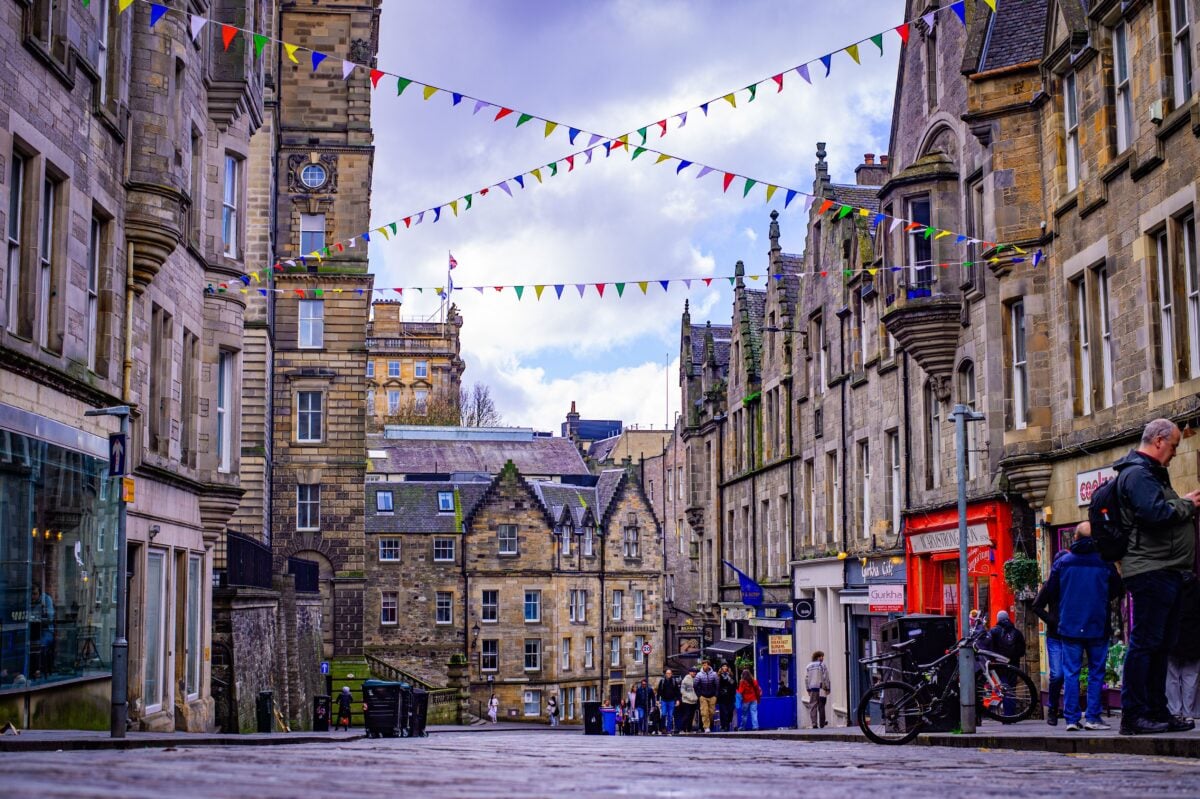 Lively Edinburgh street lined with historic architecture and festive bunting above. Perfect depiction of Scottish urban charm.