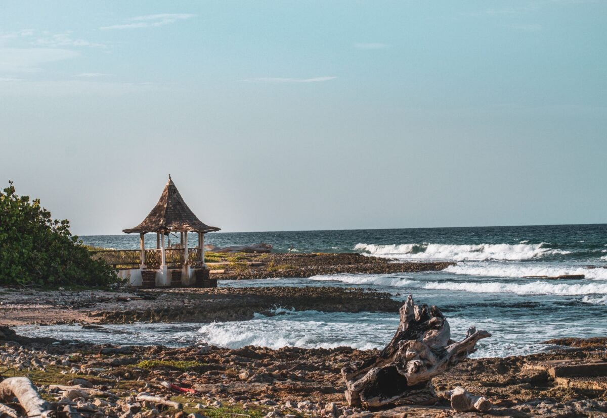 pexels 5005126 | Two Scots Abroad A picturesque beach scene with a gazebo by the sea, featuring waves crashing on a rocky shore.