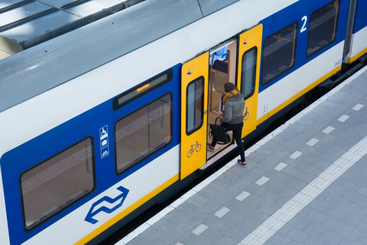 A woman boards a blue and yellow train at an outdoor railway platform, captured from above.