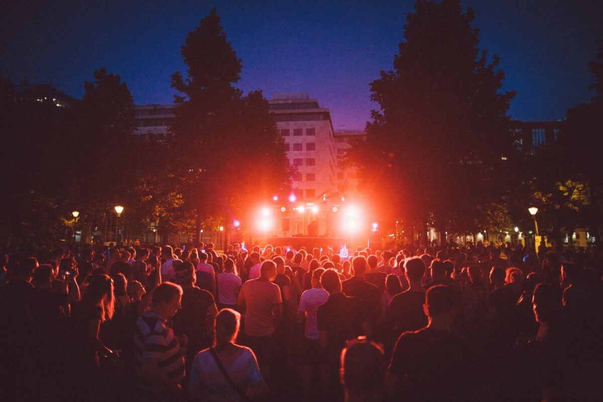 A lively outdoor EDM festival at night with a DJ and a vibrant crowd under colorful lights.