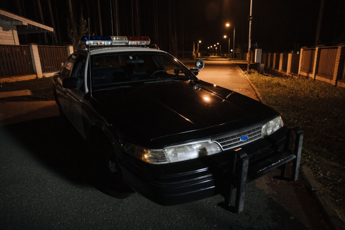 pexels 10466471 | Two Scots Abroad A police car parked on a quiet street at night with streetlights illuminating the road.