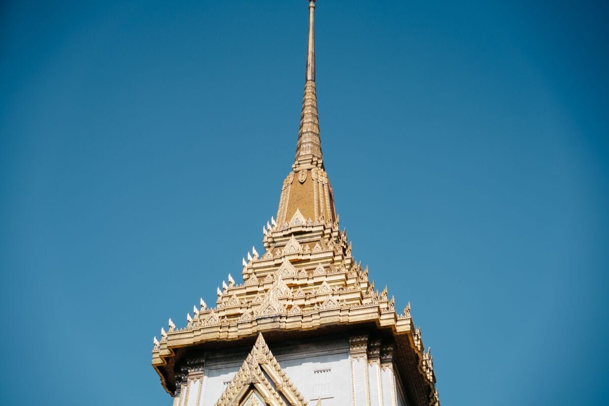 pexels 12111008 | Two Scots Abroad Low angle view of the golden spire of Wat Traimit temple in Bangkok under a clear blue sky.