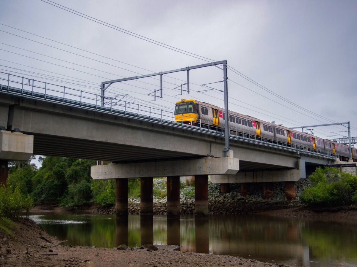 pexels 12286410 | Two Scots Abroad A passenger train travels across a concrete bridge spanning a calm river surrounded by greenery.