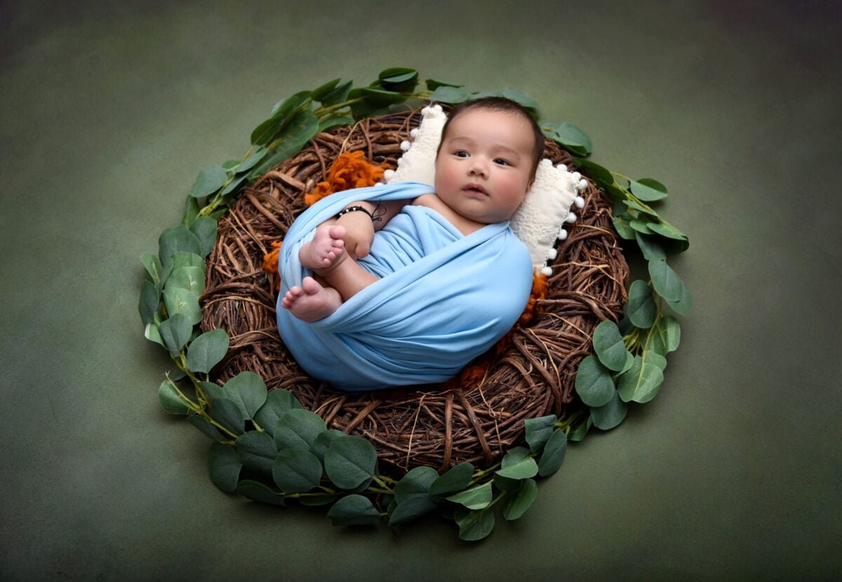 pexels 12654862 | Two Scots Abroad Cute baby wrapped in blue blanket, lying in a nest surrounded by leaves.