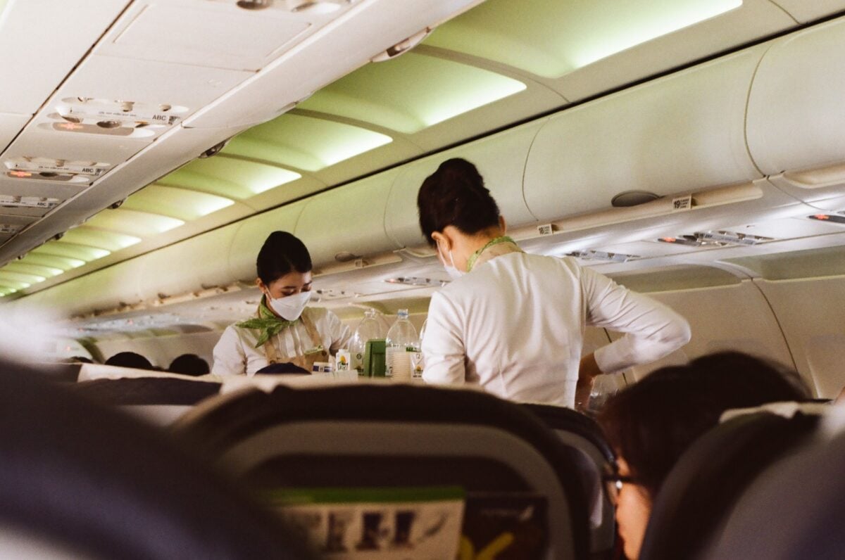 pexels 12870864 | Two Scots Abroad Flight attendants in white uniforms and masks serving passengers onboard a Vietnam airplane.