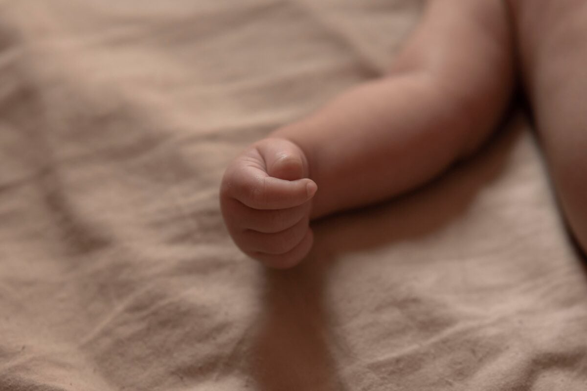 pexels 15511328 | Two Scots Abroad A delicate newborn's hand curled up on a soft beige blanket, capturing innocence.