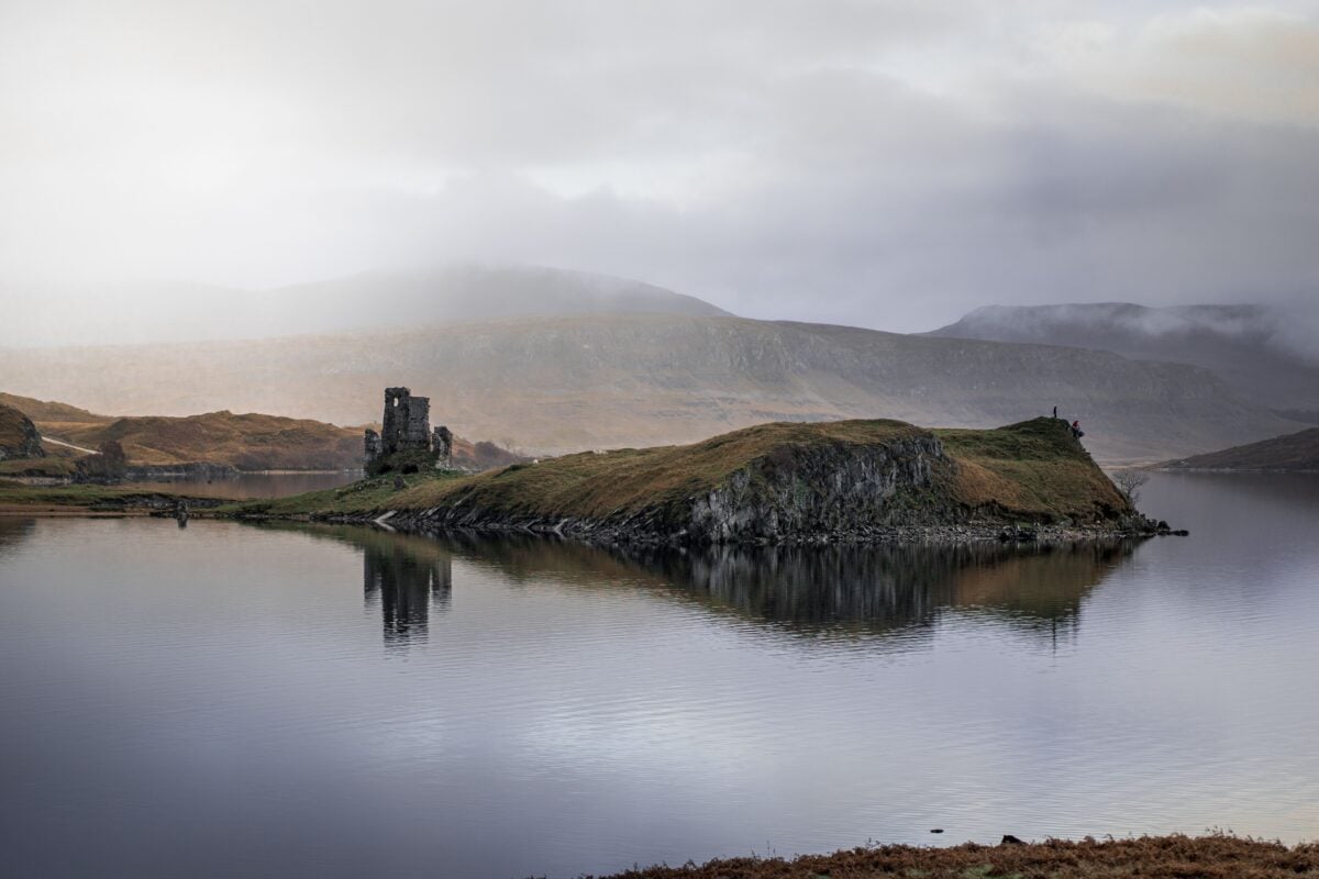 pexels 18510494 | Two Scots Abroad Scenic view of Ardvreck Castle ruins reflected on a calm Loch Assynt with misty mountains.