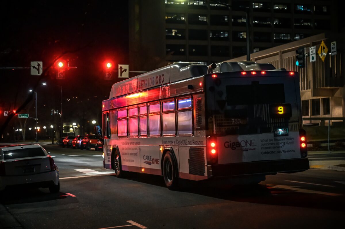 pexels 1878359 | Two Scots Abroad A city bus stopped at a traffic light during the night in an urban downtown setting.