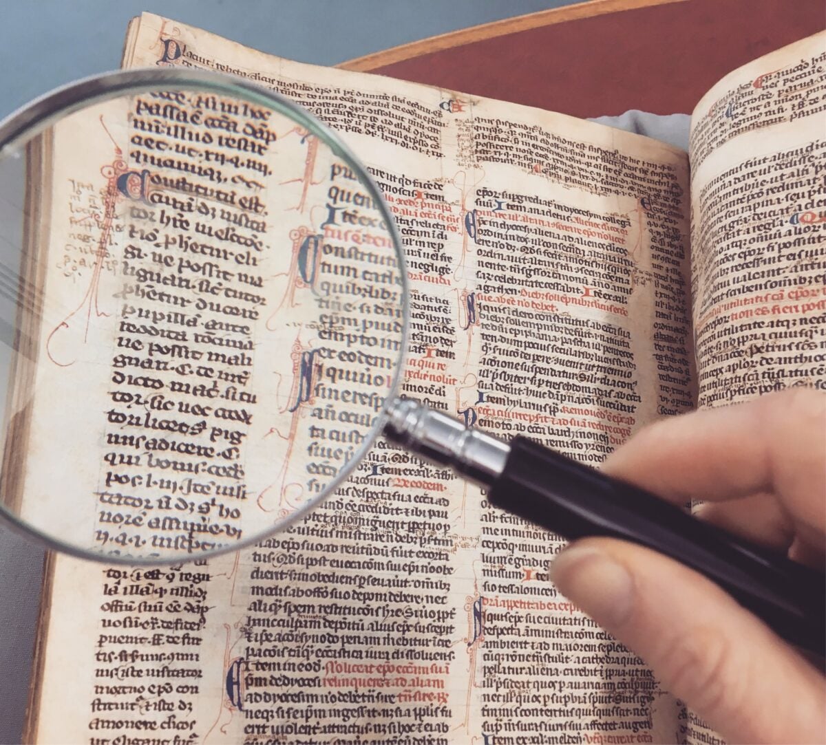 pexels 207681 | Two Scots Abroad A hand holding a magnifying glass over an antique book page, revealing intricate text and design.