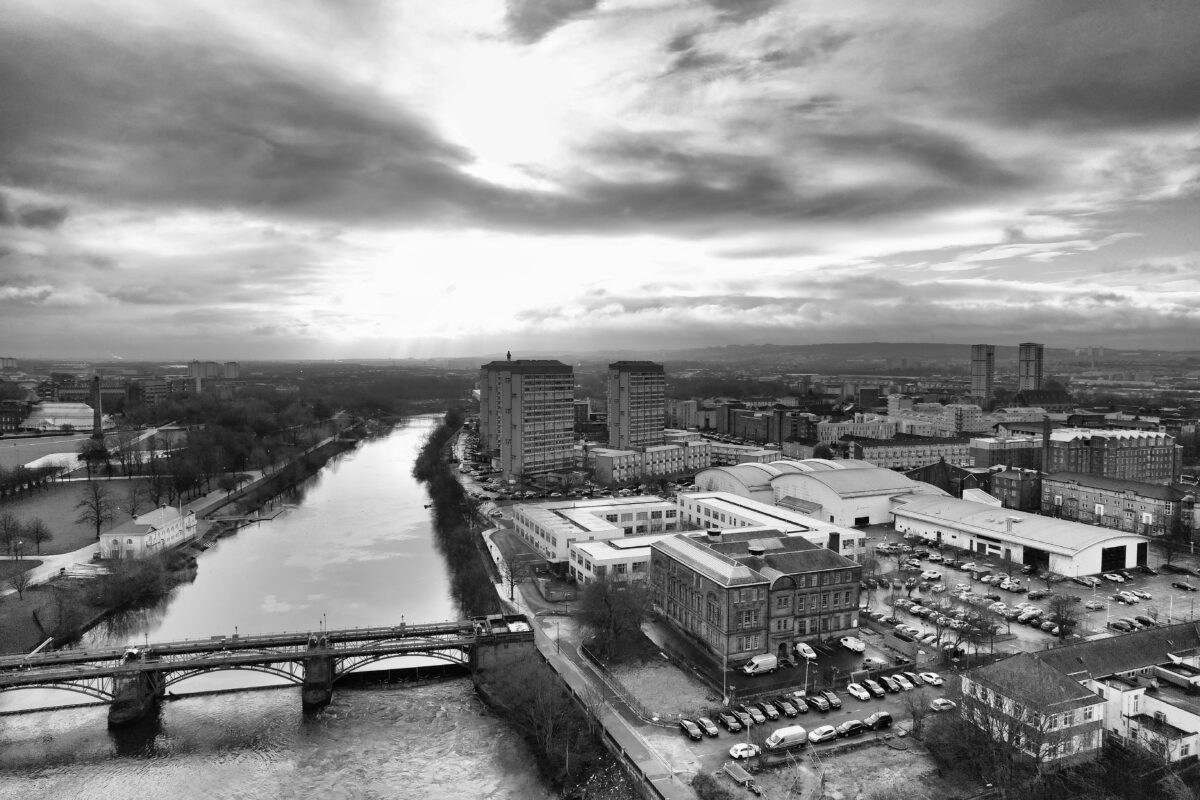 Aerial view of Glasgow's skyline with river, bridge, and dramatic clouds in black and white.