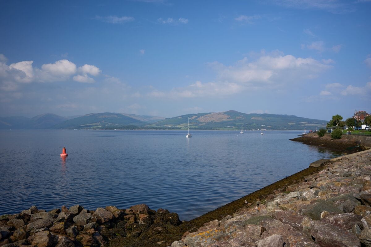pexels 34643130 | Two Scots Abroad A tranquil view of the coastline at Rothesay, Scotland, with distant hills and calm waters under a blue sky.