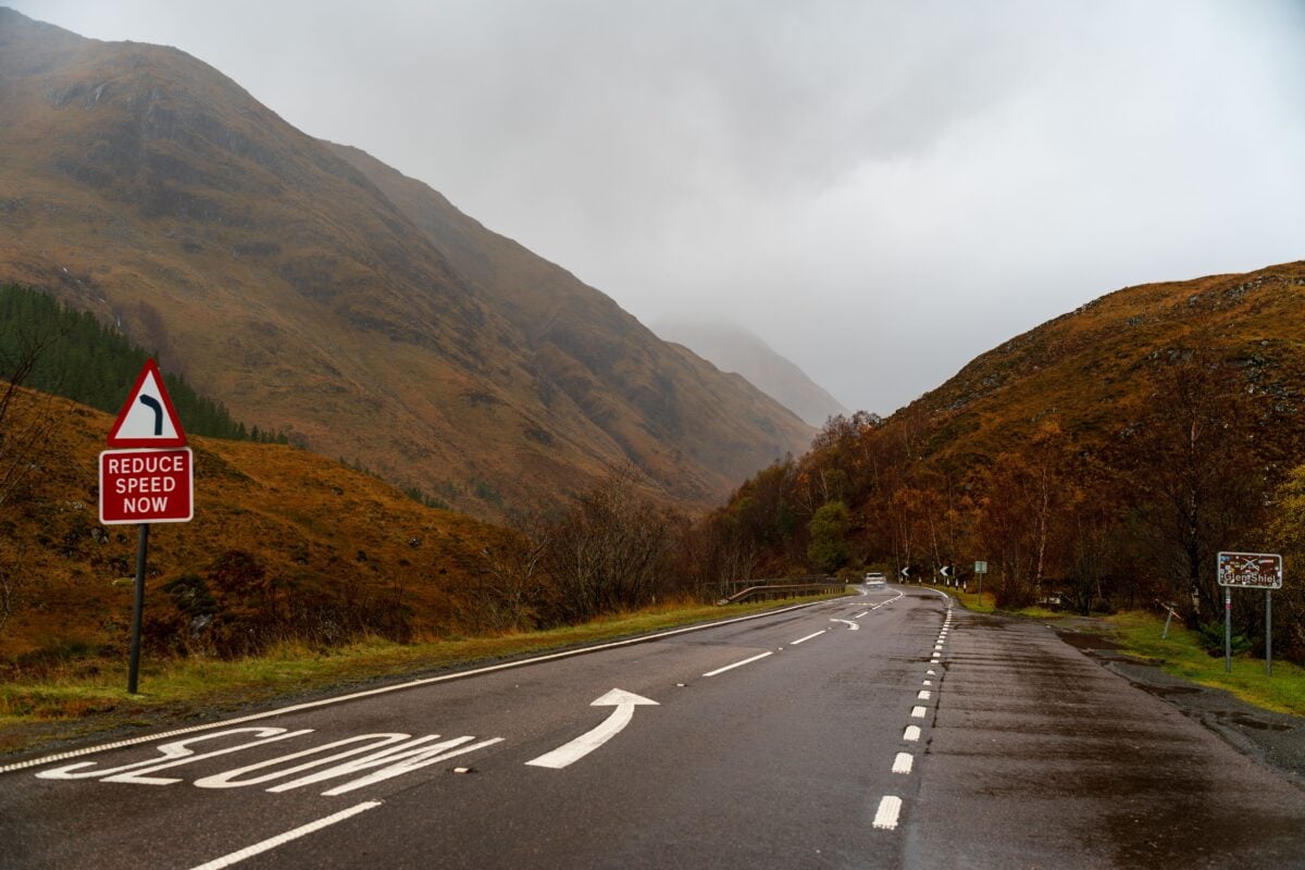 pexels 34649629 | Two Scots Abroad A winding road in the Scottish Highlands during autumn with a reduce speed sign and foggy mountains.