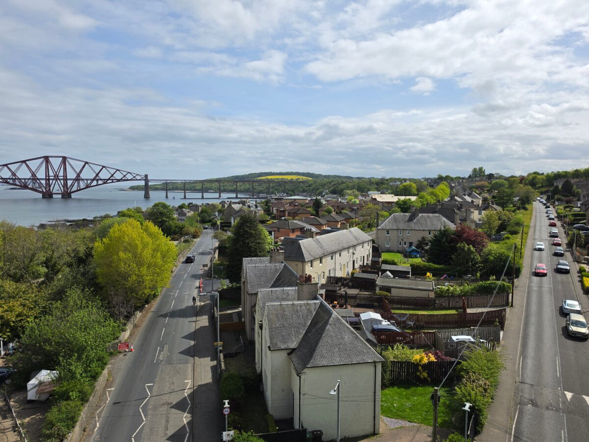 A picturesque aerial view of the village with Forth Bridge, under a partly cloudy sky.