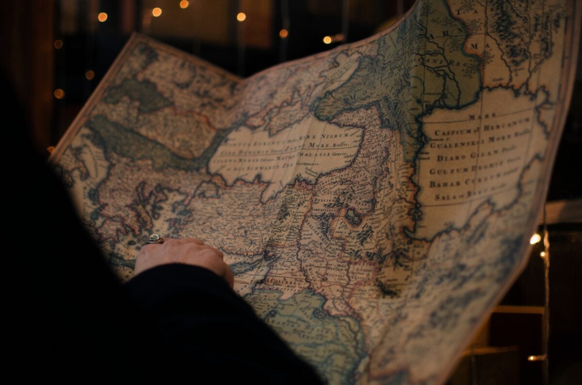 pexels 4402272 | Two Scots Abroad From behind anonymous person examining antique world map printed on large paper in blue colors in dark room
