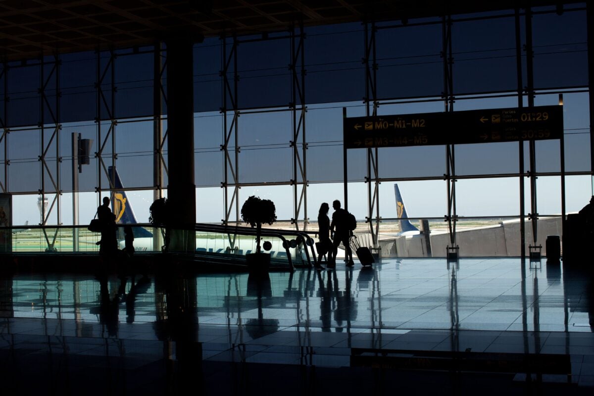 pexels 4671911 | Two Scots Abroad Travelers silhouetted in a modern airport terminal with glass windows and visible airplane tails.