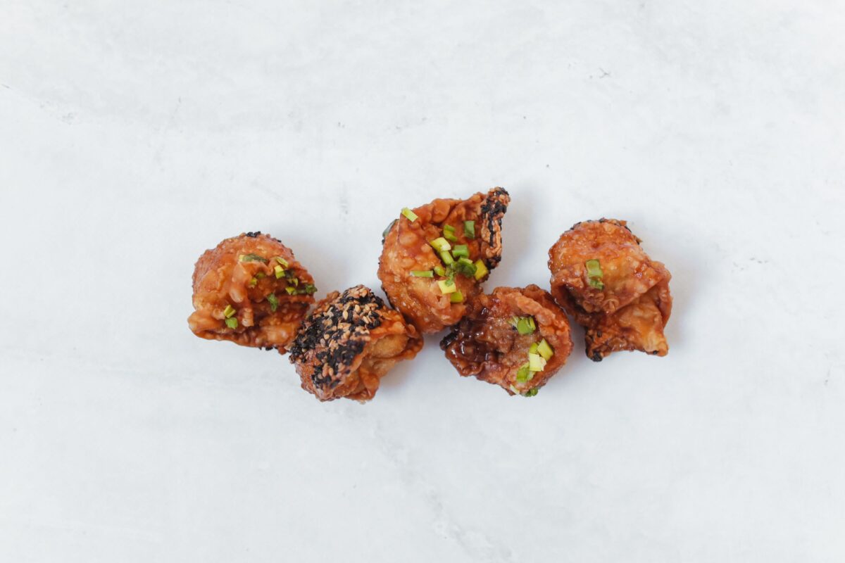 Top-down view of crispy fried dumplings garnished with spring onions on a white surface.