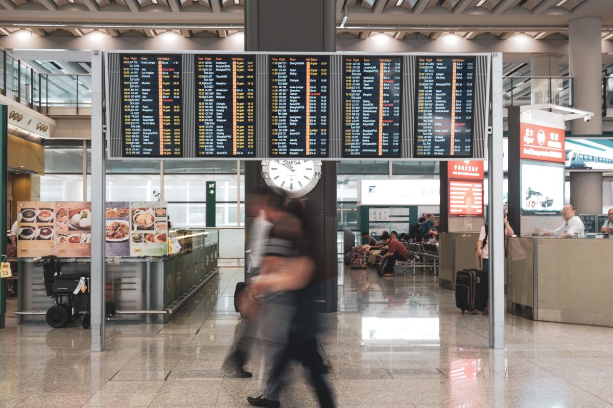 pexels 6544058 | Two Scots Abroad Blurred motion of travelers in a modern airport terminal with departure screens and a prominent clock.