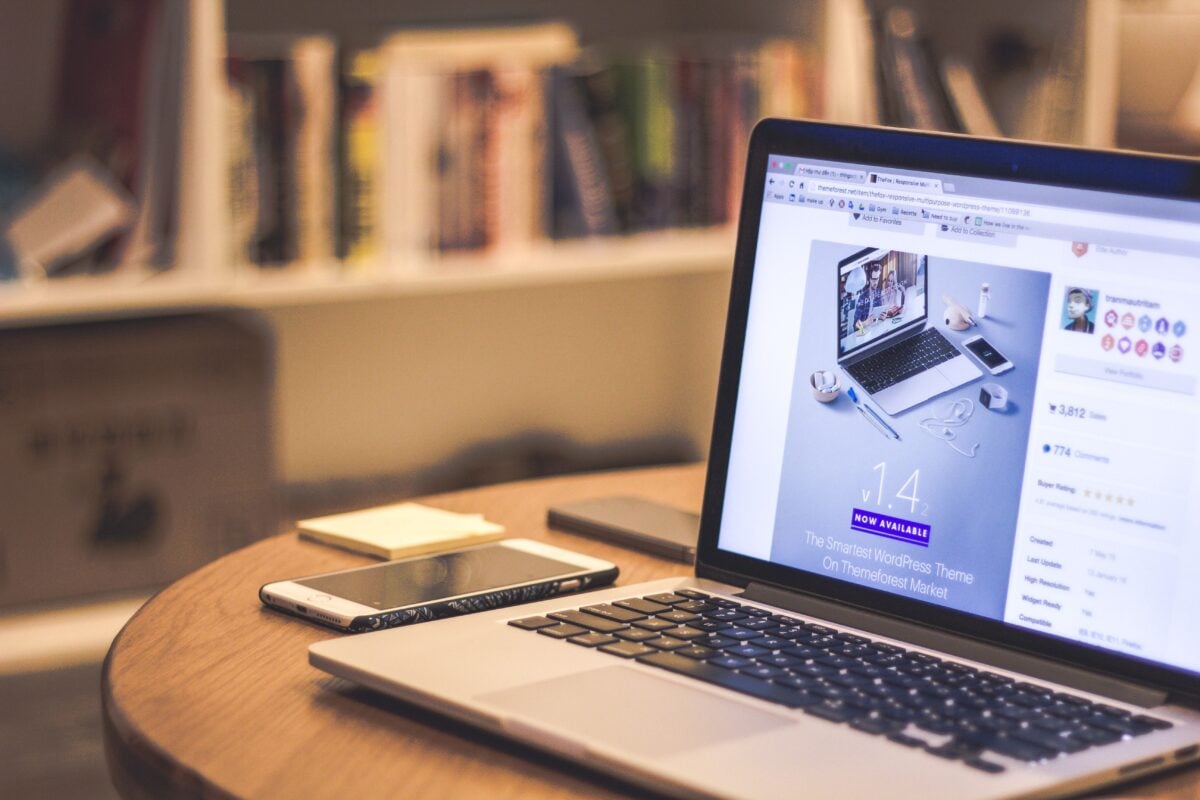 pexels 69432 | Two Scots Abroad A cozy modern workspace featuring a laptop displaying a website, a smartphone, and books on shelves.