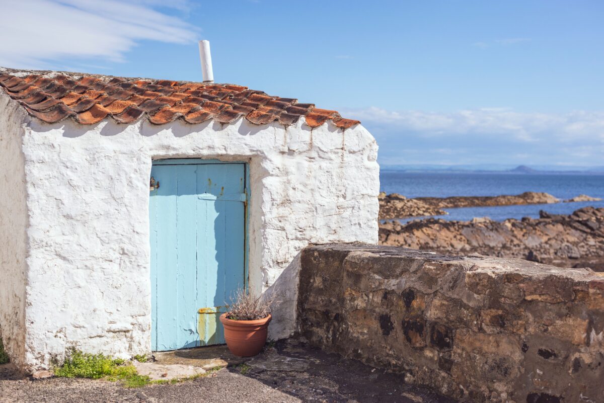 pexels 8425458 | Two Scots Abroad Charming white seaside cottage with a blue door, set against the coastal landscape of Pittenweem, Scotland.