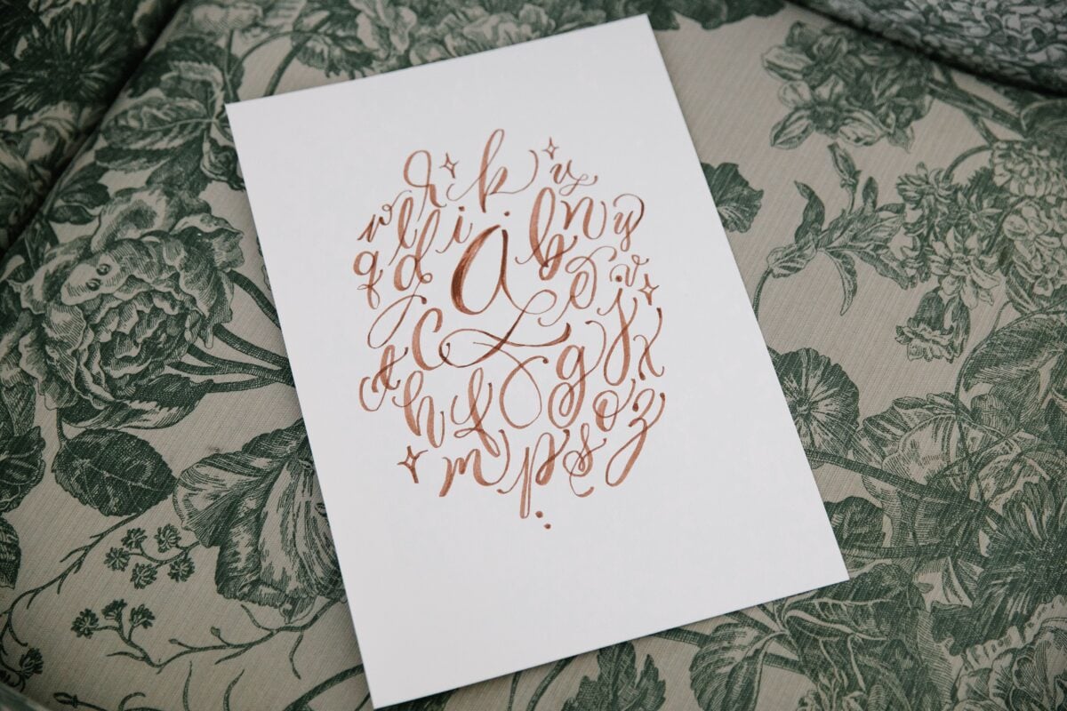 pexels 8715875 | Two Scots Abroad A beautiful handwritten alphabet on paper placed on a floral textile background, showcasing artistic calligraphy.
