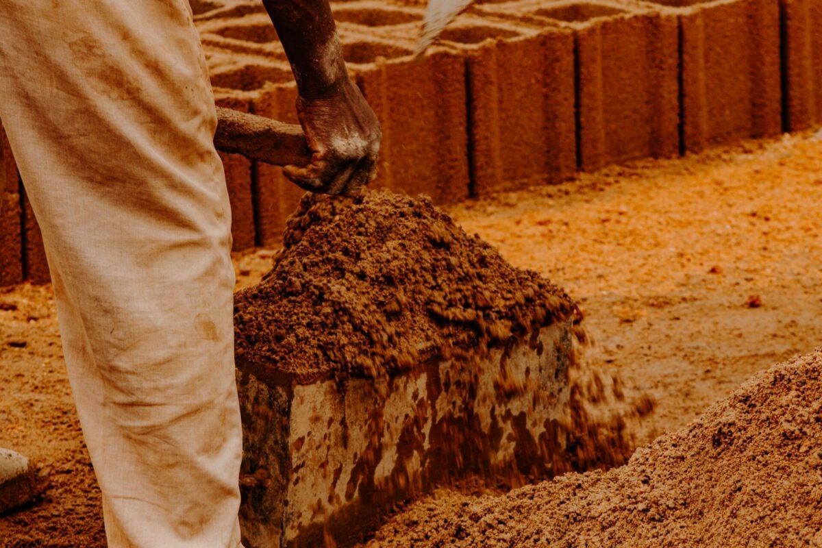 pexels 33894660 | Two Scots Abroad A worker shaping clay to mold bricks outdoors under natural sunlight.