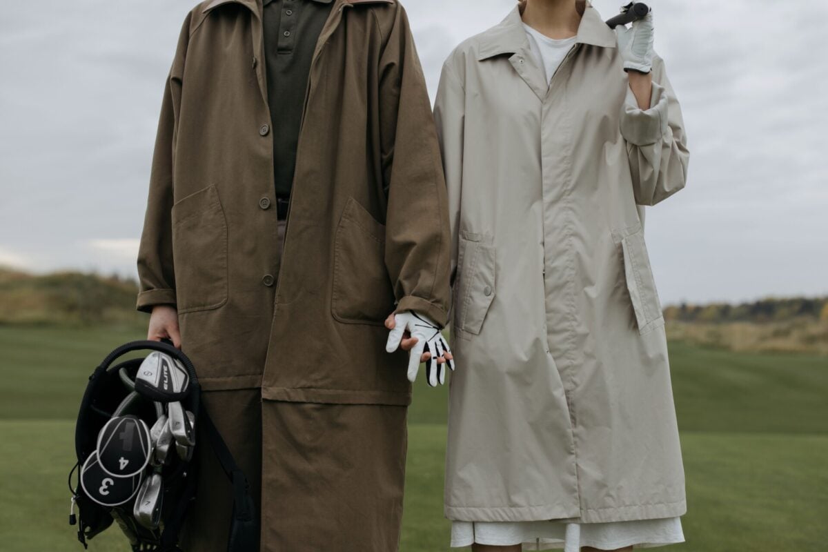 pexels 6256054 | Two Scots Abroad Couple standing on a golf course holding hands and golf bag, wearing long coats.