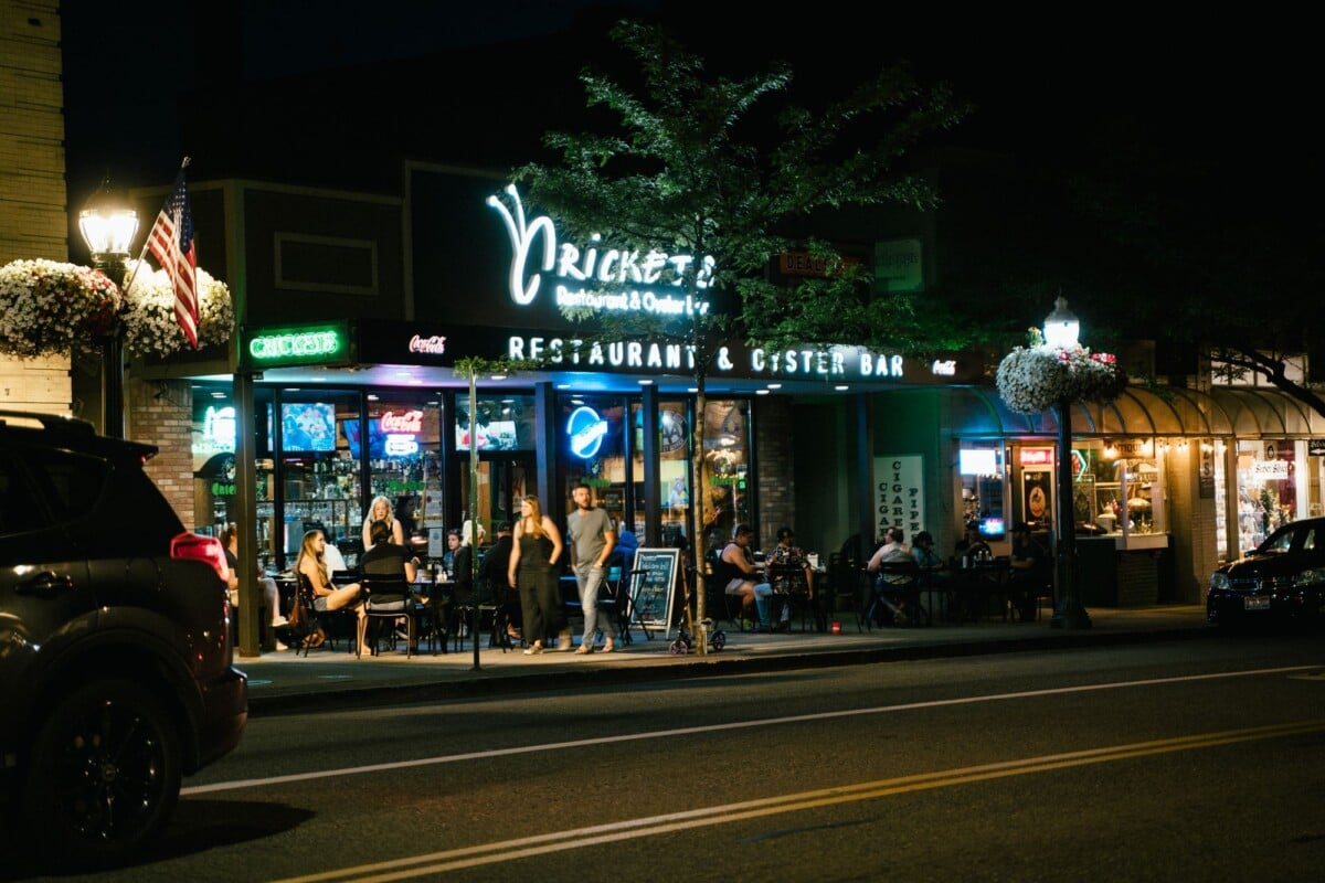 A bustling urban nightlife scene at a restaurant and oyster bar, with people dining outside.