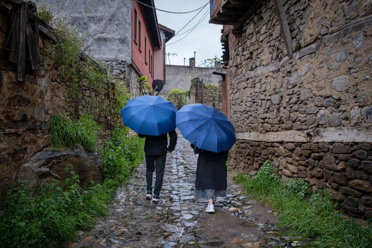 A couple with blue umbrellas strolls down a historic stone alleyway, surrounded by aged architecture.