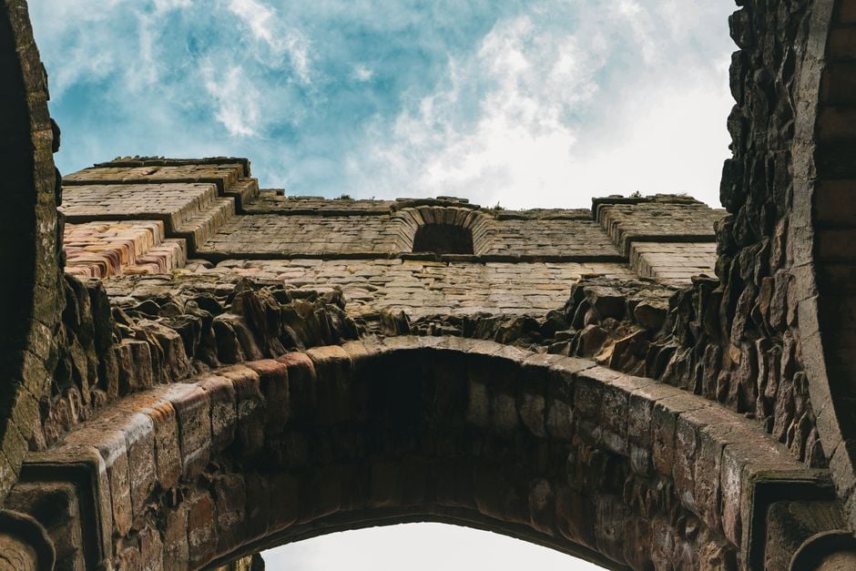 A detailed view of an ancient stone archway ruin set against a cloudy blue sky.
