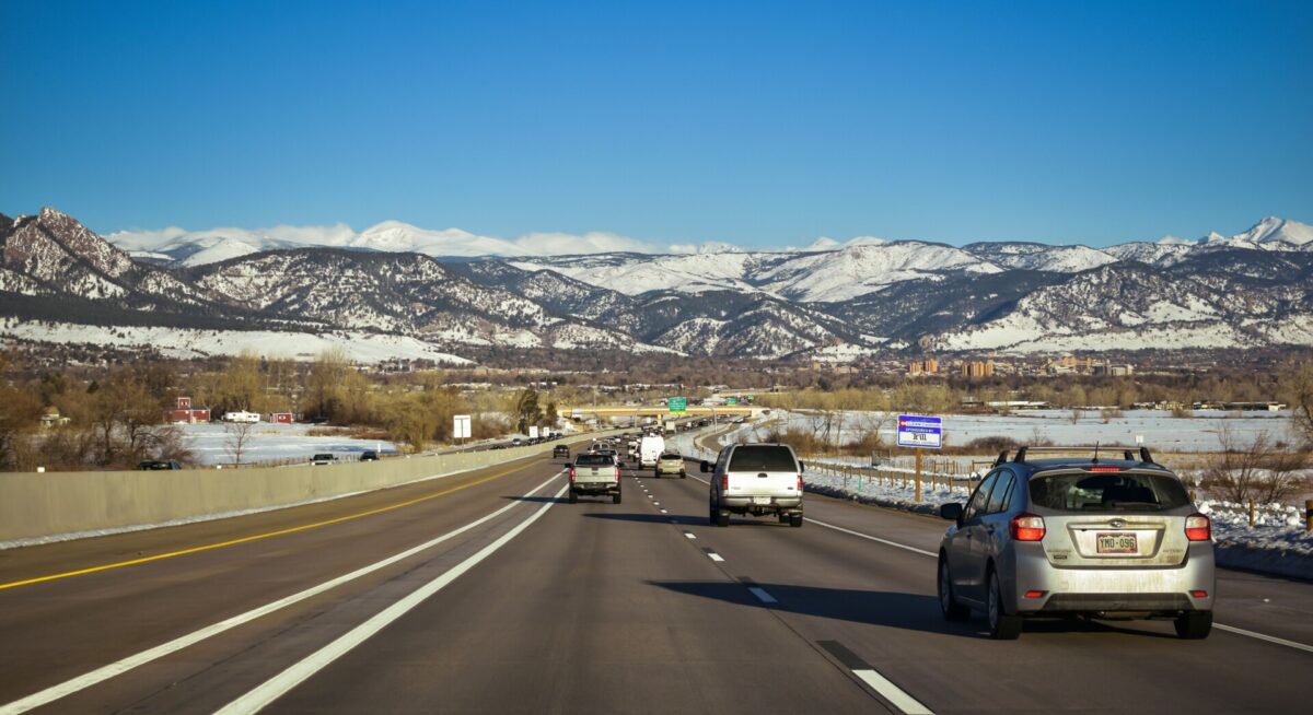 A scenic highway view surrounded by snow-capped mountains under a clear blue sky, showcasing traffic flow in Colorado.