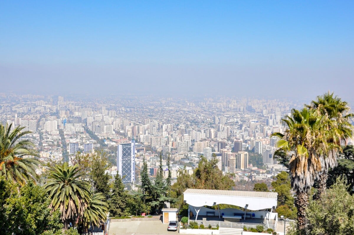 A scenic view of Santiago, Chile from Cerro San Cristobal with city skyline and palm trees.