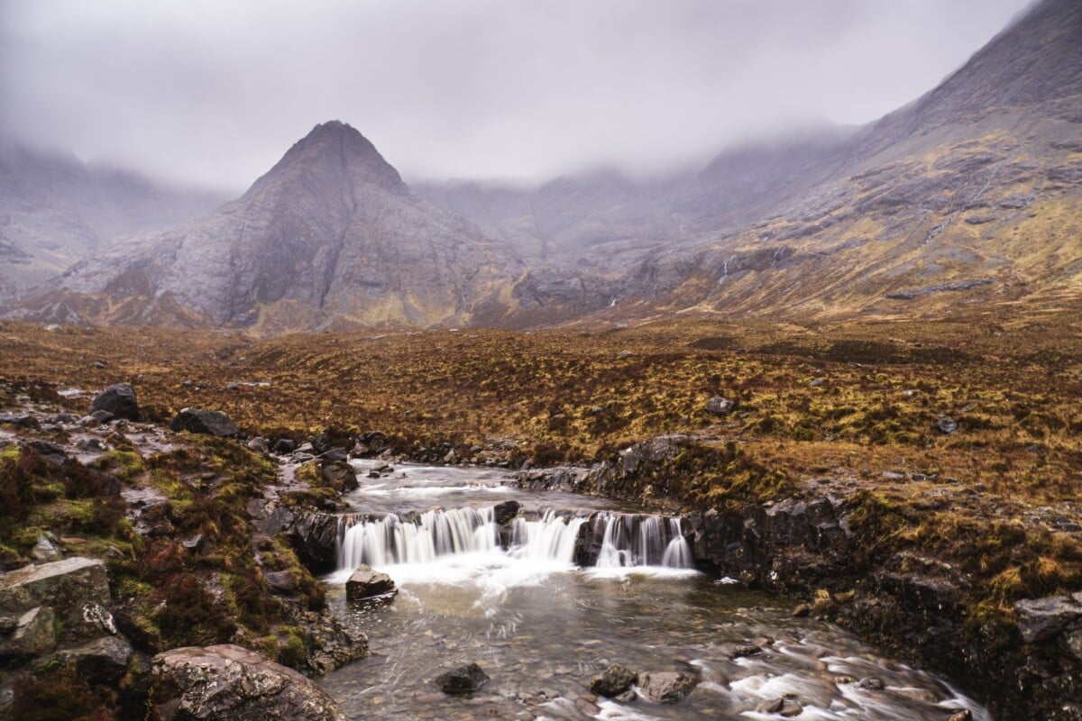A scenic waterfall in the misty Scottish Highlands with towering mountains.