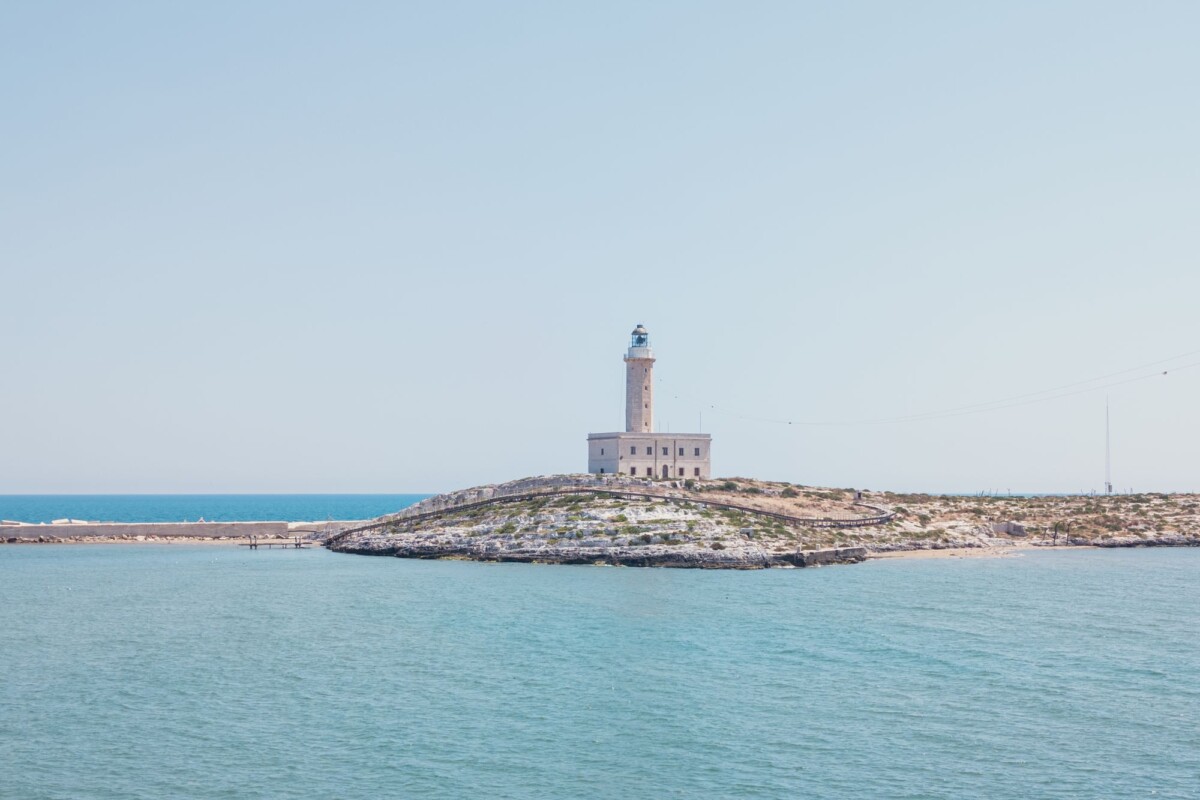 A serene view of a lighthouse on a rocky coastal island under a clear blue sky.
