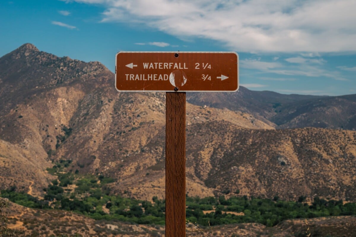 A wooden signpost indicating trail directions with a stunning mountain backdrop.