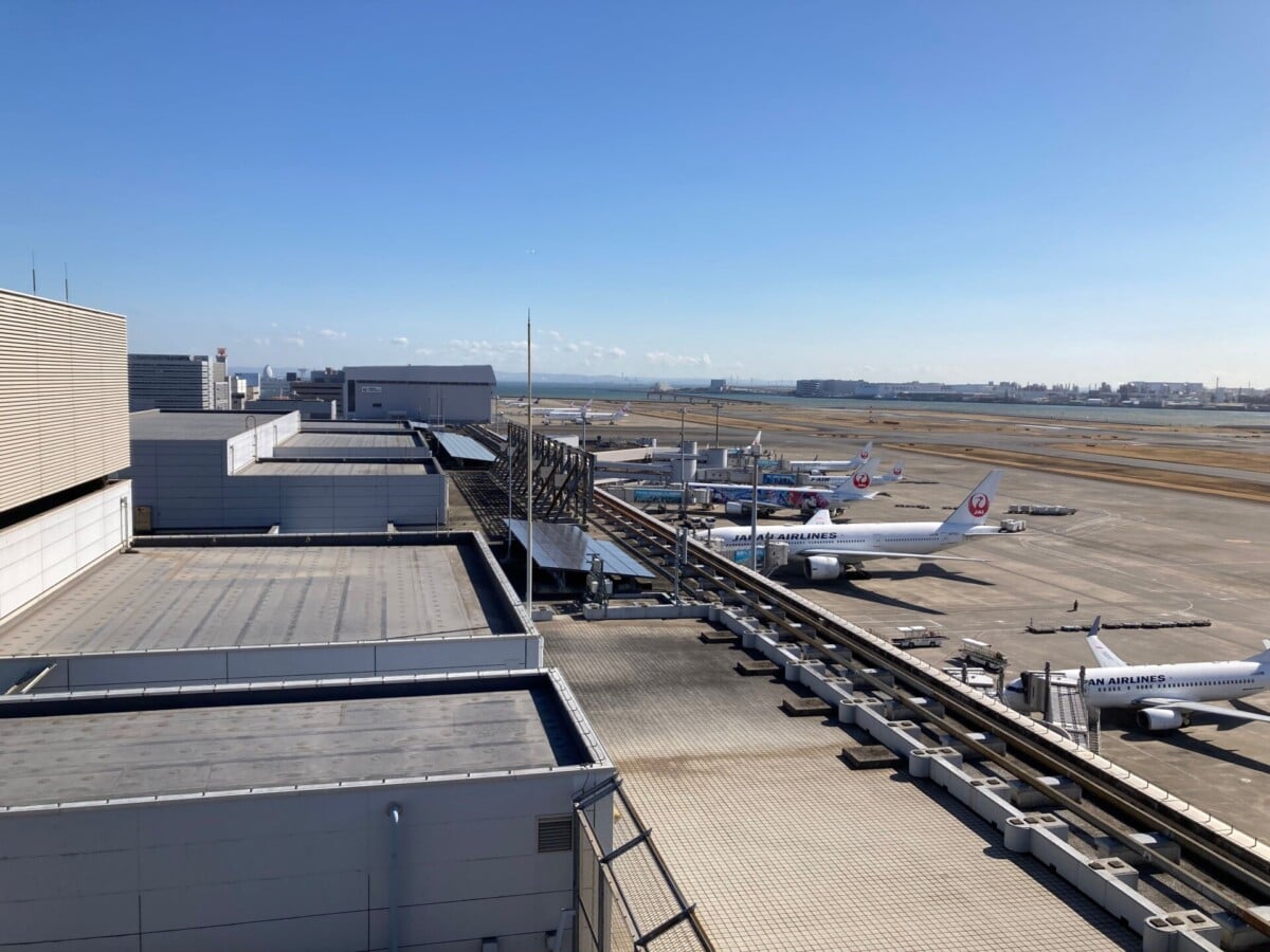aerial view of haneda airport with several airplanes parked at the terminal gate | Two Scots Abroad Aerial view of Haneda Airport with several airplanes parked at the terminal gates under clear blue skies.