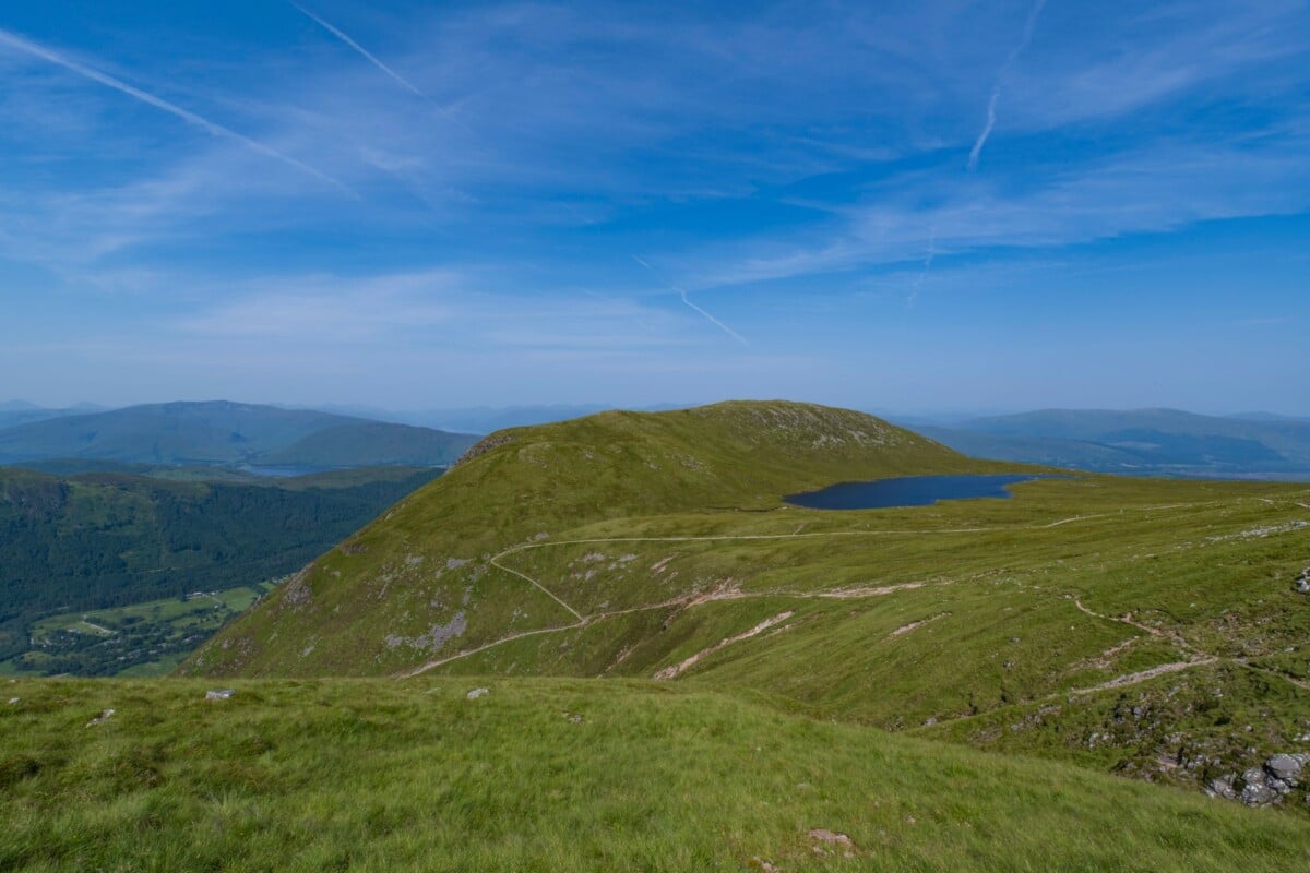 Breathtaking view of the Scottish Highlands with rolling hills, a serene loch, and expansive blue skies.