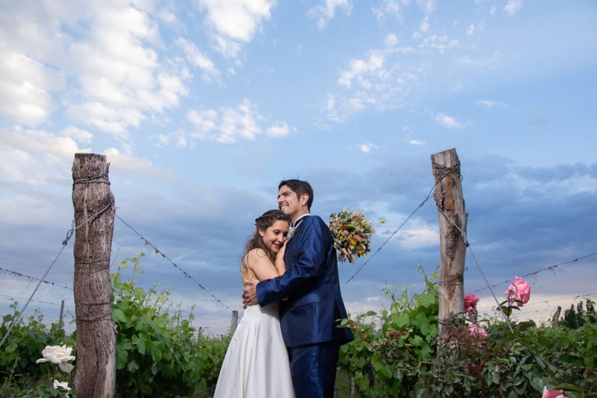 Bride and groom embrace outdoors in a vineyard, captured during sunset.