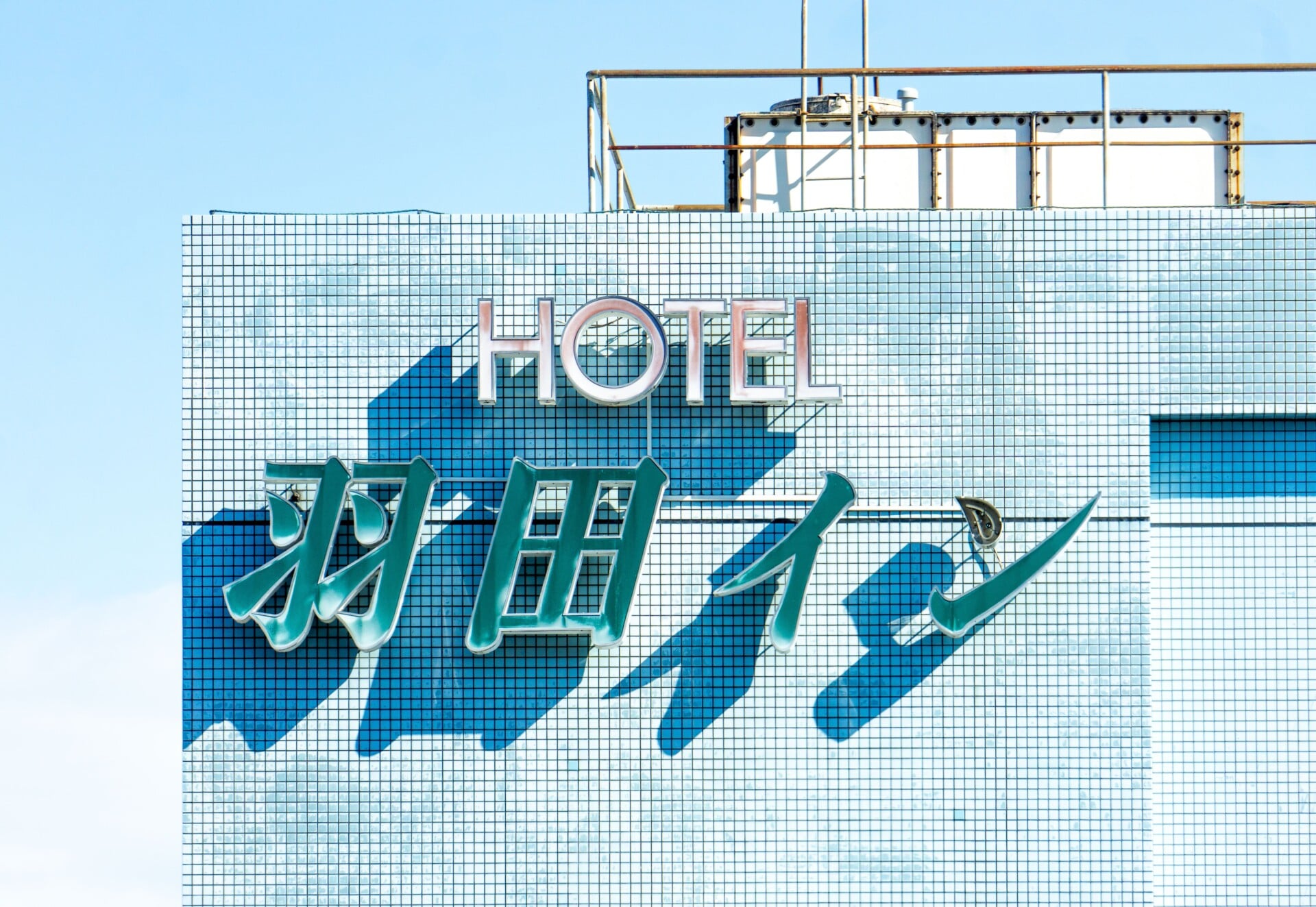 brightly lit hotel sign with blue tiles under a clear sky showcasing modern arch | Two Scots Abroad Brightly lit hotel sign with blue tiles under a clear sky, showcasing modern architecture.