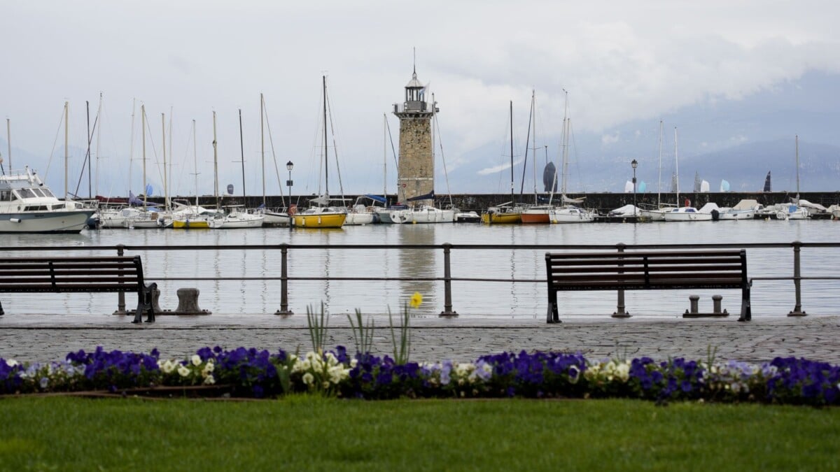 Captivating view of Desenzano del Garda lighthouse and marina, featuring lush flowers and serene water.