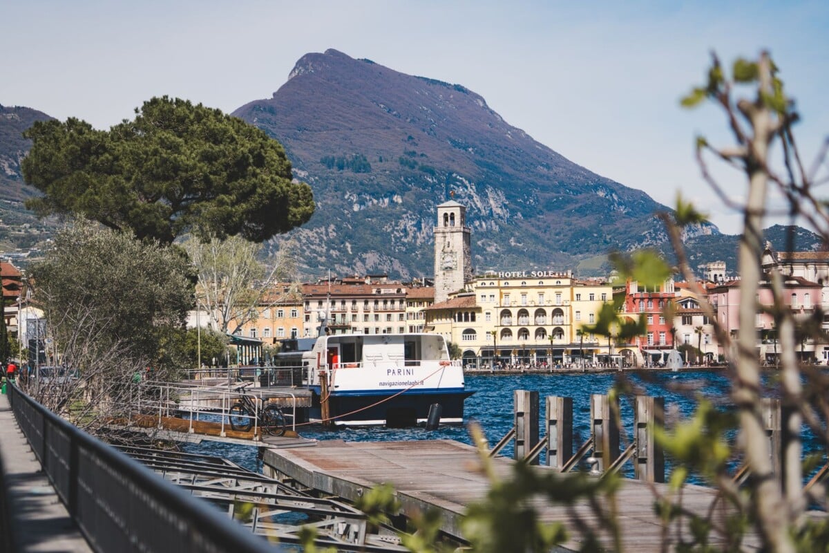 Charming lakeside town of Riva del Garda with picturesque mountains and a boat docked at the pier.