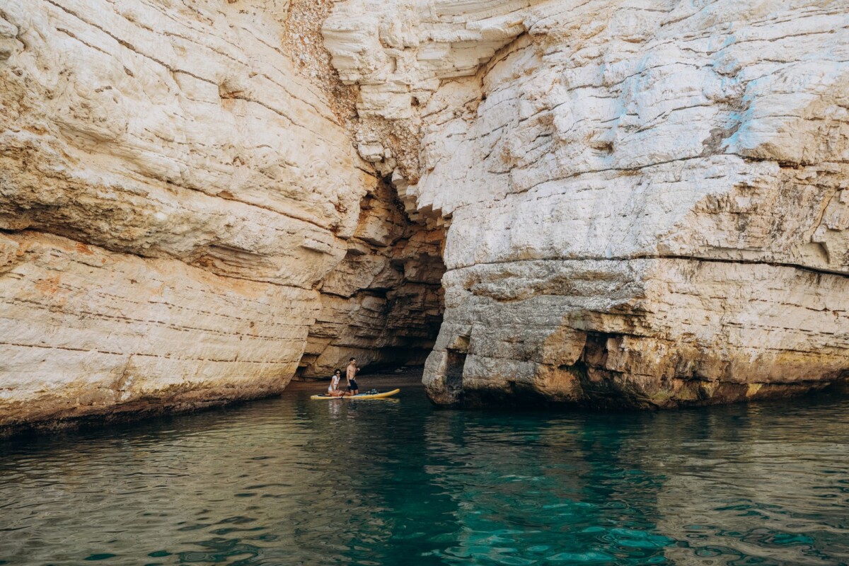 Kayakers explore a stunning limestone cave in Vieste, Puglia, during summer.
