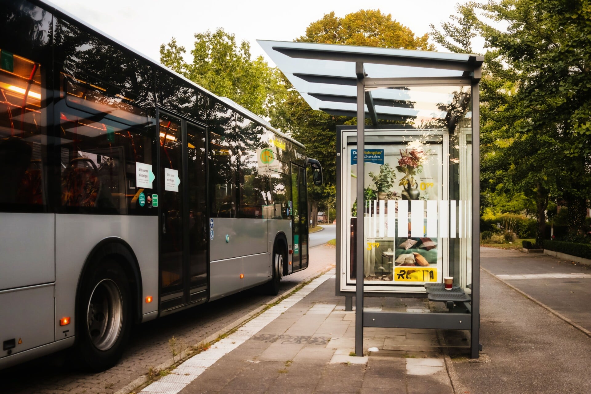 Modern city bus at a glass bus stop during summer, showcasing urban transportation and greenery.