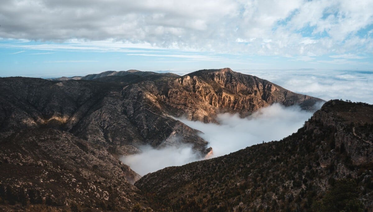 stunning view of a mountain range enveloped by rolling clouds under a bright sky | Two Scots Abroad Stunning view of a mountain range enveloped by rolling clouds under a bright sky.