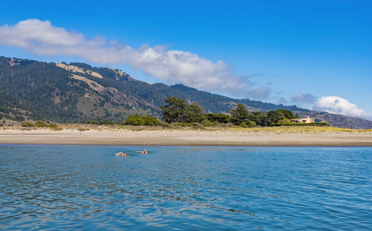 Swimmers enjoy a sunny day at a serene beachfront with a mountainous backdrop.